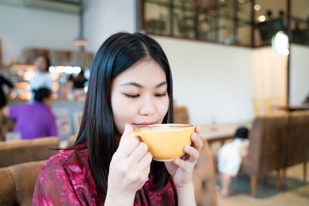 Beautiful asian women hold hot latte art coffe cup sitting in cafe Business women