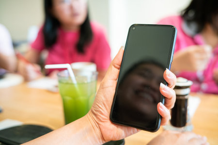 Mockup image women hands holding mobile phone with blank black screen in busy restaurant blurred people backgroundの写真素材
