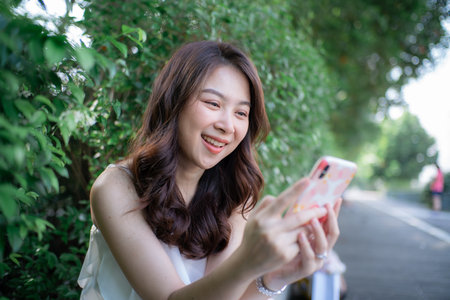 Portrait of beautiful hipster smiling young woman reading  message in smartphone in city parkの写真素材
