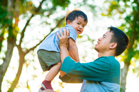 Father hold and lifting little boy in city park sunset light blurred green forest backgroundの写真素材