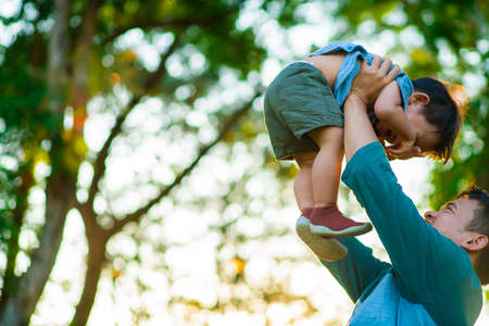 Father hold and lifting little boy in city park sunset light blurred green forest backgroundの写真素材