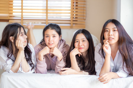 Group of four asian women lying on bed smile look at camera feels happy  friends or teenage girls having fun in cozy room at homeの写真素材