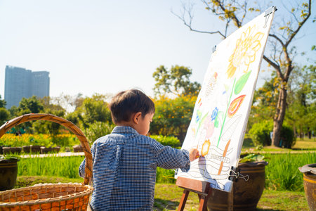 Asian kid boy drawing paint on paper in flower outdoor parkの写真素材