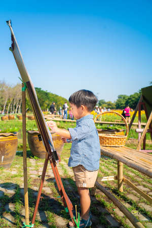 Asian kid boy drawing paint on paper in flower outdoor parkの写真素材