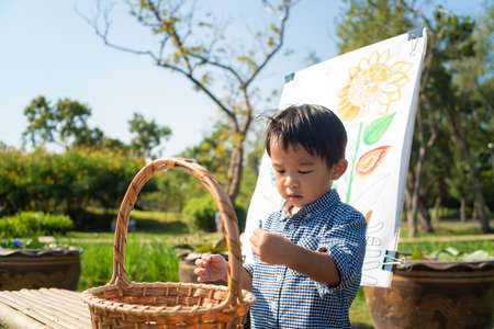 Asian kid boy drawing paint on paper in flower outdoor parkの写真素材