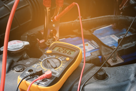 Mechanic hand use multimeter voltmeter to check the voltage level in a car battery.