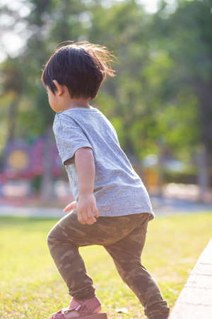 Little asian boy playing outdoor kid having fun enjoy walking on green grass of playground in the parkの写真素材