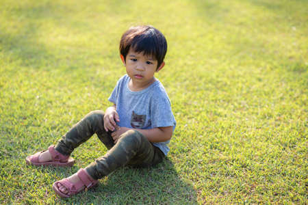 Portrait of adorable little boy sitting on green meadow grass morning light city park boy in natureの写真素材