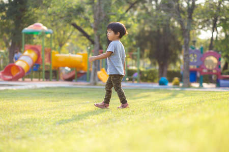 Little asian boy playing outdoor kid having fun enjoy walking on green grass of playground in the parkの写真素材