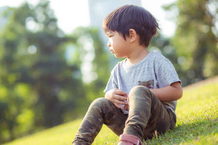 Portrait of adorable little boy sitting on green meadow grass morning light city park boy in natureの写真素材