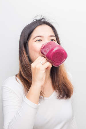 Woman drinking healthy fruit vegetable berry juice smoothie made of super foods fruits and berries on white backgroundの写真素材