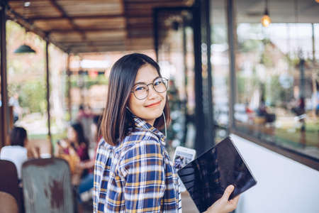 Smiling young asian glasses woman hold digital tablet in hands in cafeの写真素材