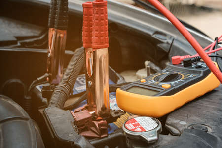Mechanicl man uses electric multimeter voltmeter to check the voltage level maintenance car battery