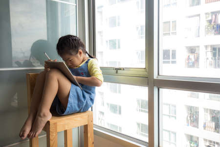 Preschool girl using tablet computer relax in cozy room online educationの写真素材