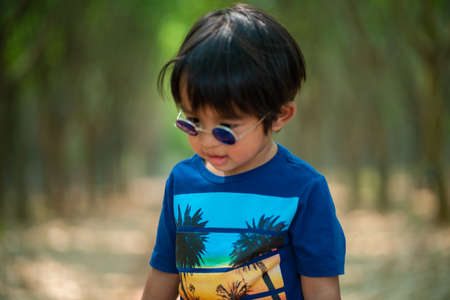 Portrait of happy little boy wear sunglasses playing in green forest park outdoor fashionの写真素材