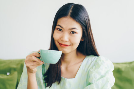 Beautiful women sittingon green sofa drink hot latte coffee aroma drinkの写真素材