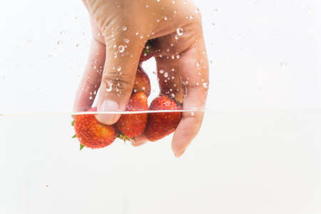 Hand pick up fresh strawberry fruit in water on white backgroundの写真素材