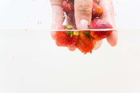 Hand pick up fresh strawberry fruit in water on white backgroundの写真素材