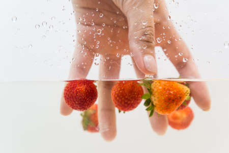 Hand pick up fresh strawberry fruit in water on white backgroundの写真素材