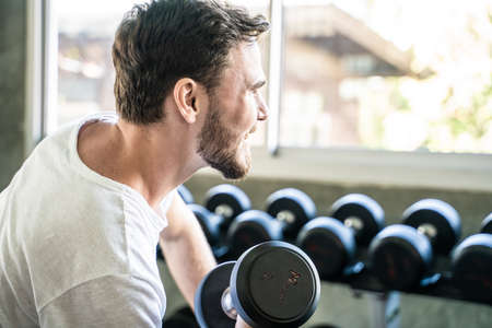 Sport man lifting up dumbbell sitting in private sport gym social distanctingの写真素材