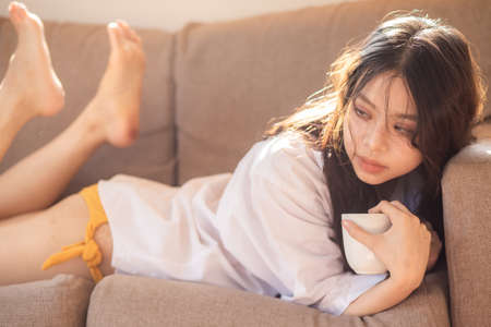 Pretty women with coffee cup lying on sofa light of window relax womenの写真素材