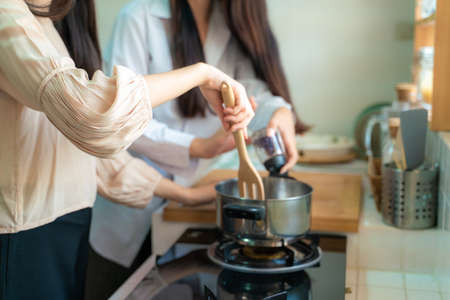 Young female asian women friends cooking in kitchen preparing together meal at home