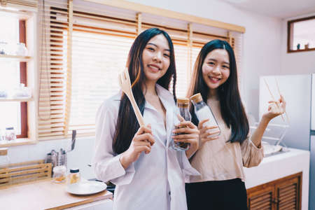 Young female asian women friends cooking in kitchen preparing together meal at homeの写真素材