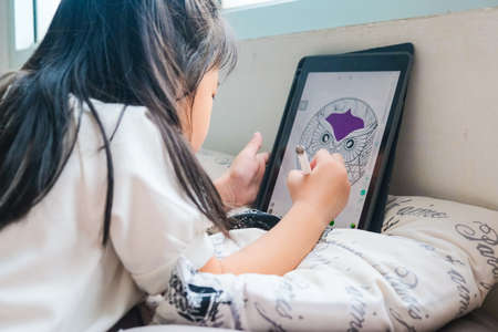 Little school girl drawing cartoon graphic on tablet computer online student working from homeの写真素材