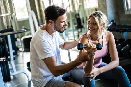 Sport women lifting dumbbell with trainer men in gym body builderの写真素材