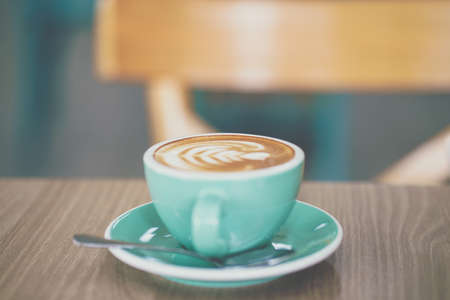 Hot latte art in green ceramic cup on wooden table with art texture beverage businessの写真素材