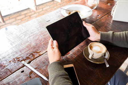 Man shows screen of digital blank tablet device over a wooden with coffee workspace tableの写真素材