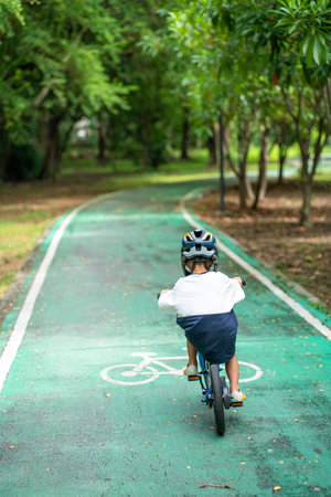 Asian kindergarten boy practice ride bicycle in city park tree forest outdoor exerciseの写真素材