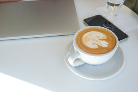 Hot latte art coffee with phone and laptop on white table document stationary objectの写真素材