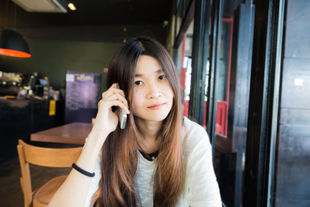 Asian beautiful women talking on smart phone while sitting in cafe, Business women with cellphoneの写真素材