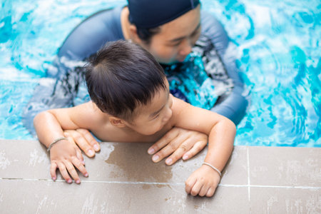 Happy kindergarten asian boy swimming with mom in condominium swimming pool outdoor activityの写真素材