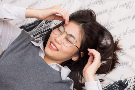 Glasses women relax lying on bed white blanketの写真素材