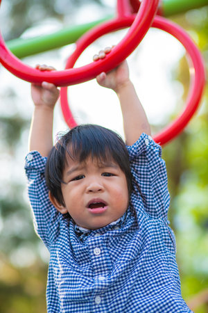 Little 2 - 3 year asian boy climbing on bar in outdoor playground city park happy boyの写真素材