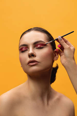 Beautiful young woman makes shine on her face using makeup brush on the yellow background. Caucasian...