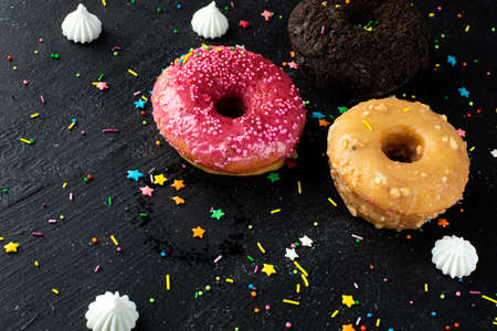 Three sweet donuts lie on a black wooden table with powder and marshmallows