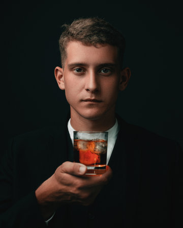 Tasting, tasting. A man in a suit holds a glass of brandy. Tasting and wine tasting concept. Young businessman in an elegant suit with a glass of whiskey. Sommelier tastes an expensive drinkの写真素材