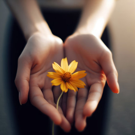A hand holding a yellow flower extends to you.の素材