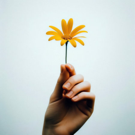 A hand holding a yellow flower extends to you.の素材