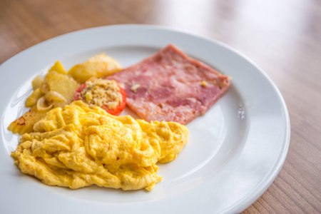 Breakfast with scrambled eggs, slice pork ham, tomato, and potatoの写真素材