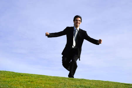successful and happy young adult businessman running and jumping in the green fieldの写真素材