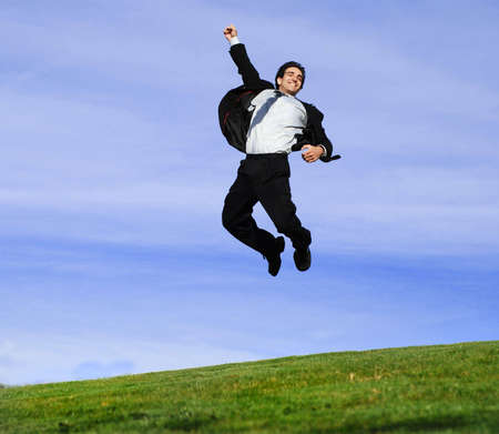 successful and happy young adult businessman running and jumping in the green fieldの写真素材
