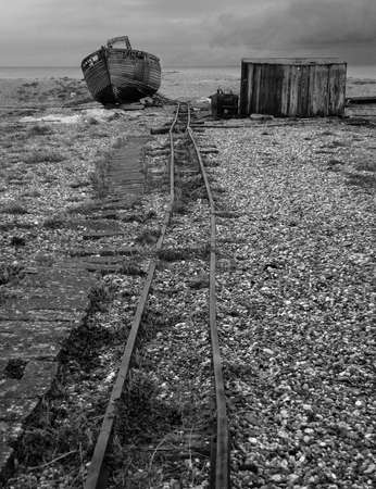 An abandoned fishing hut & fishing boat on the shingle beach of Dungeness in Kent sitting astride the a narrow gauge rail for transporting the catch from the beach to the road.の写真素材