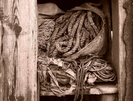 One of the abandoned fishing huts to be found on the shingle beach of Dungeness in Kent. This one is falling apart exposing its forgotten contents to the weather leaving the rope spilling from its hesian sack.の写真素材
