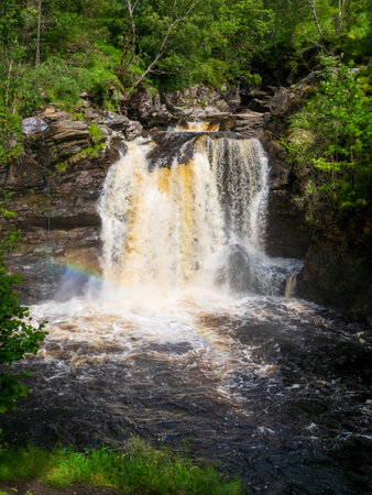 The splashing waters of the Falls of Falloch generating a rainbow in the spray rising from the surfaceの写真素材