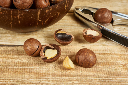 Macadamia nuts in the brown bowl and nutcracker on wooden table, close-up