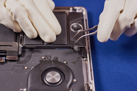 Master in white gloves dismantles the connector using tweezers. Laptop in aluminum case on a blue velvet background. Close-upの写真素材